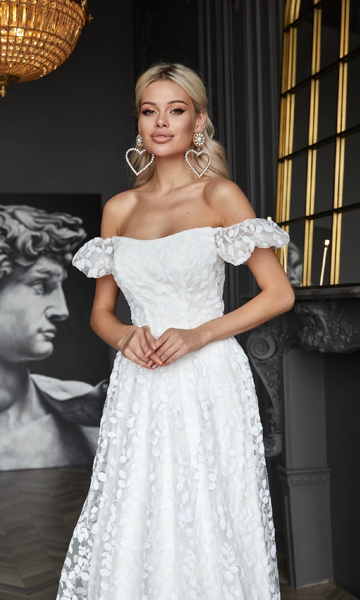A woman in the Long White Lace Formal Dress: Tina Holly TK023W stands indoors near a large classical statue and ornate decor.